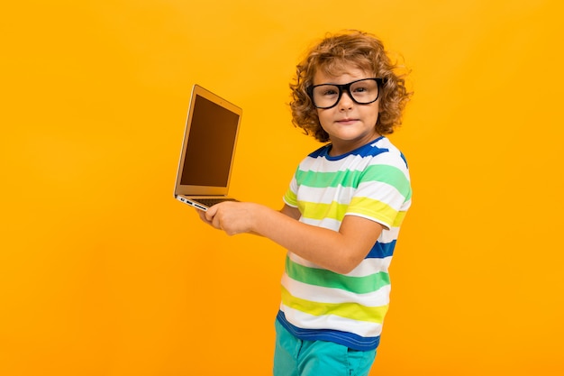 Niño pequeño con el pelo rizado en coloridos camiseta y pantalones cortos tiene un portátil aislado en amarillo