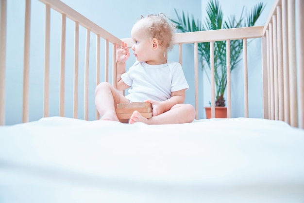 Niño pequeño de pelo rizado El niño pequeño se sienta en la cama y mira a su alrededor. Copie el espacio.