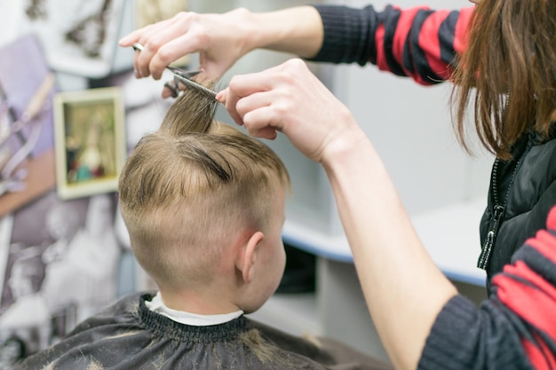 Un niño pequeño en una peluquería A un niño le cortan el pelo en la cabeza