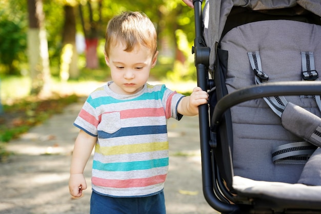 Niño pequeño pensativo se encuentra cerca del cochecito en el parque Lindo niño de un año y medio Enfoque selectivo