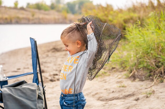 Un niño pequeño pesca y quiere atrapar el pez más grande. Niño pequeño lindo en mal estado en red. Concepto de vacaciones de verano.