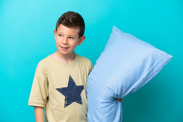Niño pequeño en pijama aislado de fondo azul mirando hacia un lado y sonriendo
