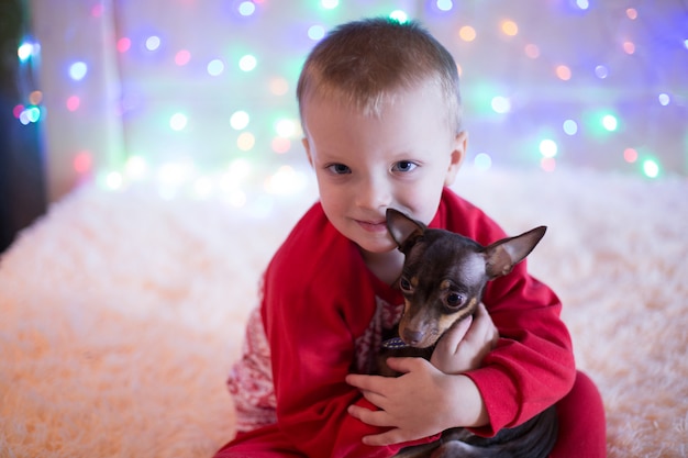 Niño pequeño en pijama rojo jugando con un perro en Nochebuena