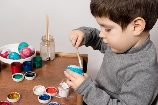 Un niño pequeño pinta huevos de gouache