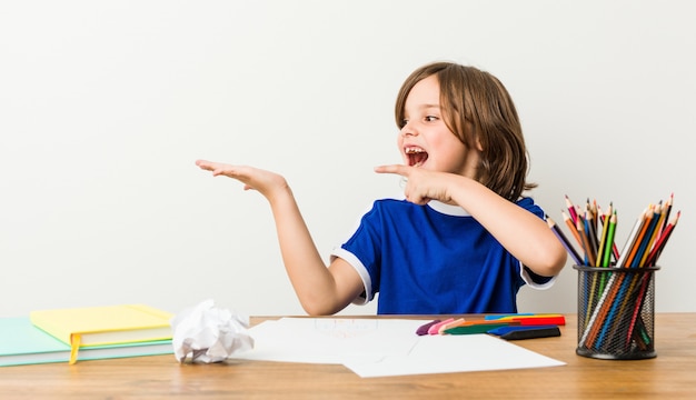 Niño pequeño pintando y haciendo la tarea en su escritorio emocionado.