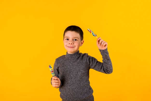 Niño pequeño con piruletas sobre un fondo amarillo