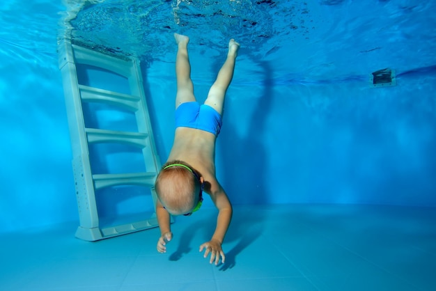 Un niño pequeño practica deportes en una piscina infantil y se sumerge desde las escaleras hasta el fondo.