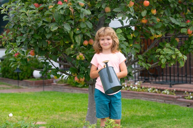 Niño pequeño preescolar activo regando plantas con lata de agua en el jardín