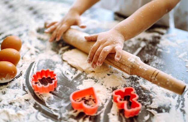 Niño pequeño preparando masa para hornear. Manos pequeñas amasando masa y masa enrollada