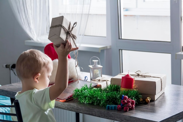 Un niño pequeño en previsión de Navidad y año nuevo levanta un regalo con las manos