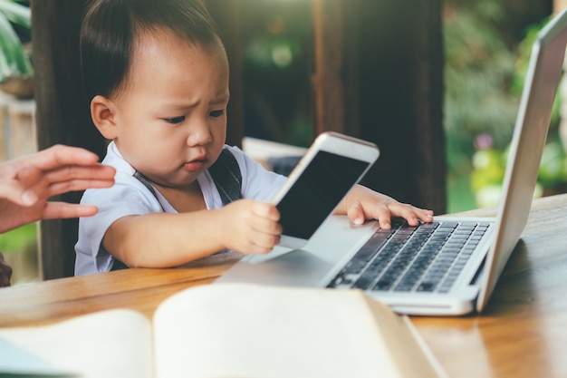 niño pequeño que aprende con el teléfono móvil, la computadora portátil, la tableta, y el libro.