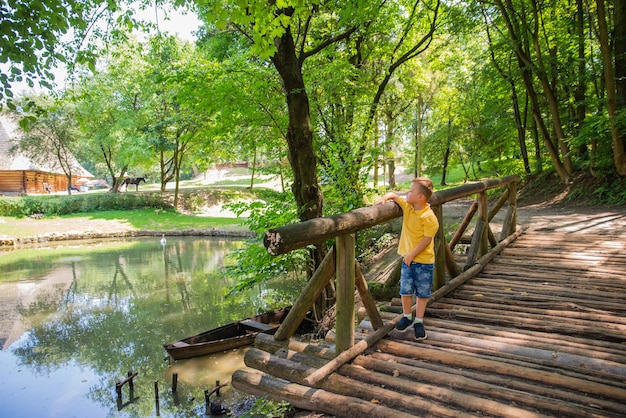 Niño pequeño que camina cerca del lago del pueblo en el puente de madera