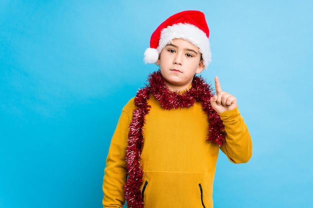 Niño pequeño que celebra el día de Navidad que lleva un sombrero de santa aislado mostrando el número uno con el dedo.