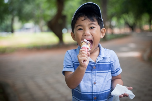 Niño pequeño que come el helado en el patio con tiempo feliz.