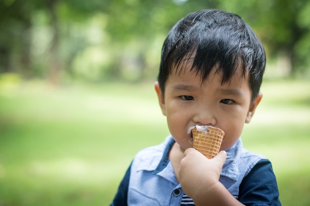 Foto niño pequeño que come el helado en el patio con tiempo feliz.