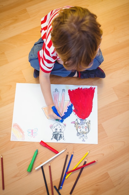 Niño pequeño que dibuja en el papel en el piso