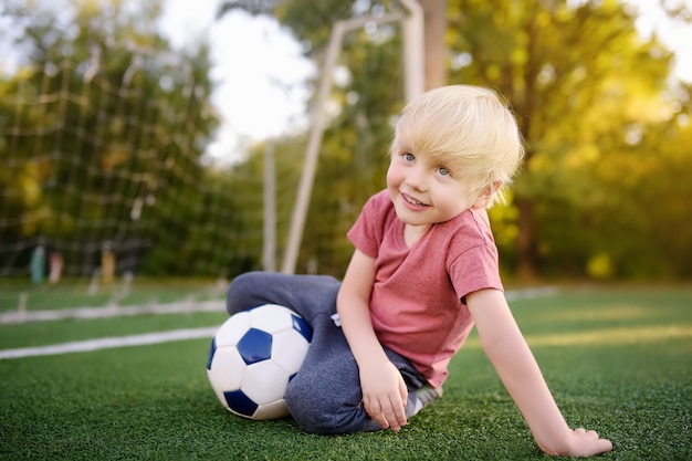 Niño pequeño que se divierte jugando un fútbol / partido de fútbol en día de verano. Juego al aire libre activo / deporte para niños.