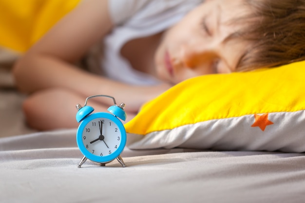 niño pequeño que duerme en la cama con un reloj despertador cerca de su cabeza