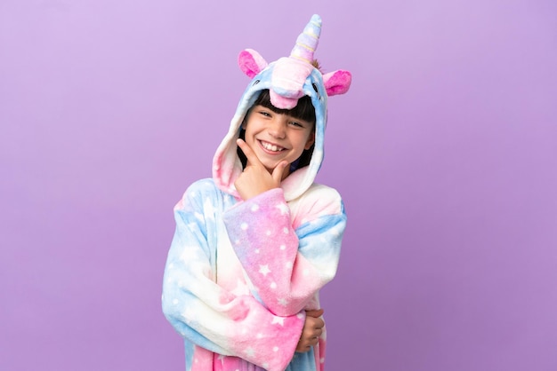 Niño pequeño que lleva un pijama de unicornio aislado en un fondo morado sonriendo