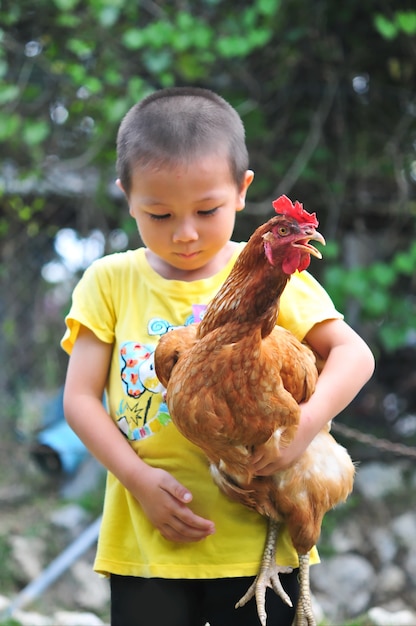 Niño pequeño que lleva un pollo en sus brazos