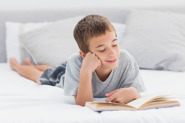 Niño pequeño que miente en el libro de lectura de la cama