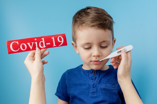 Niño pequeño que señala al papel rojo con coronavirus mesaage sobre fondo azul.