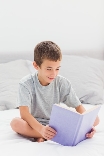 Niño pequeño que se sienta en el libro de lectura de la cama