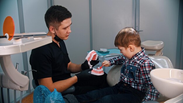 Un niño pequeño que tiene un tratamiento en la odontología moderna cepillando los dientes de un modelo plástico de mandíbulas