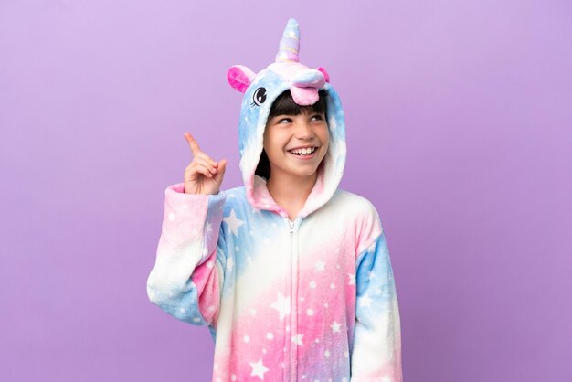 Niño pequeño que usa un pijama de unicornio aislado en un fondo morado con la intención de darse cuenta de la solución mientras levanta un dedo