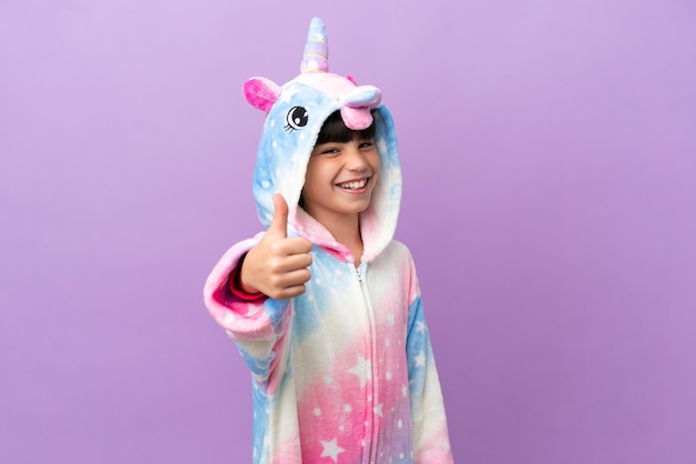 Foto niño pequeño que usa un pijama de unicornio aislado en un fondo morado con los pulgares hacia arriba porque algo bueno ha sucedido