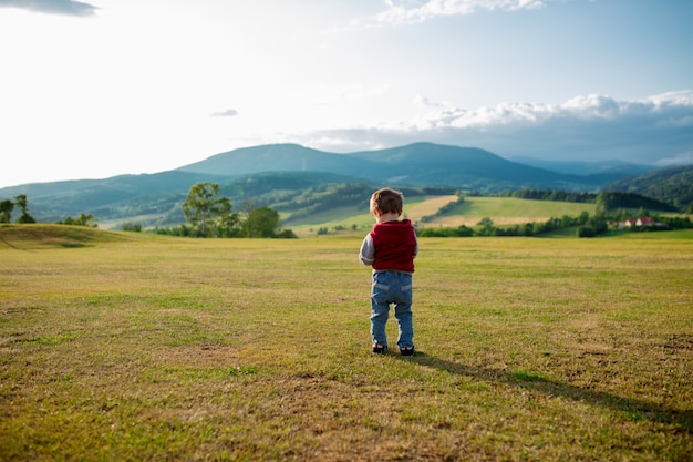 Niño pequeño quedarse en un prado en una montaña