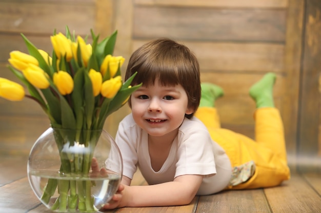 Un niño pequeño con un ramo de tulipanes amarillos. Un niño con un regalo de flores en un jarrón. Un regalo para niñas de vacaciones femeninas con tulipanes amarillos en el suelo.