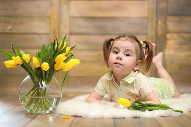 Un niño pequeño con un ramo de tulipanes amarillos. Un niño con un regalo de flores en un jarrón. Un regalo para niñas de vacaciones femeninas con tulipanes amarillos en el suelo.