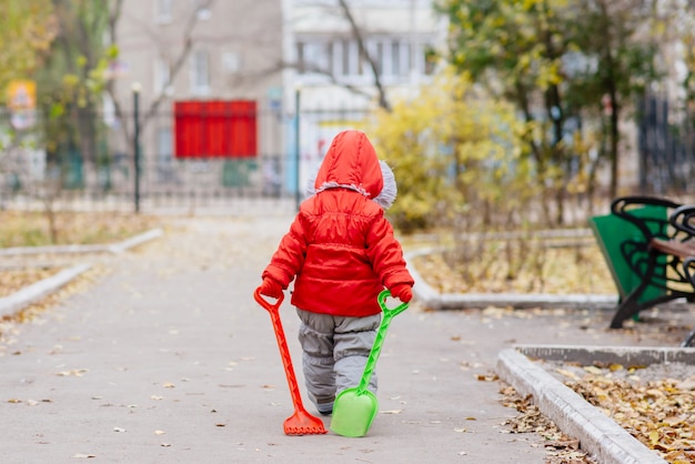 Un niño pequeño con un rastrillo y una pala camina por el parque