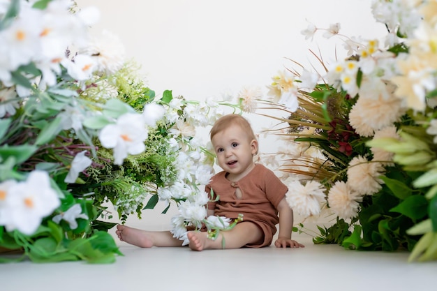 Un niño pequeño recién nacido con un traje beige se sienta en el suelo del dormitorio rodeado de hermosas flores Productos para niños