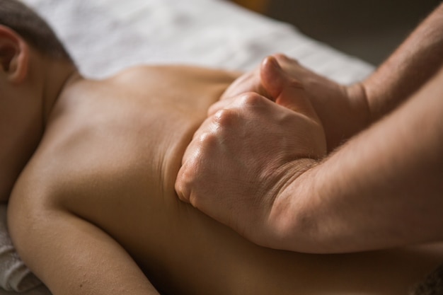 Niño pequeño se relaja con un masaje terapéutico. Fisioterapeuta que trabaja con el paciente en la clínica a la espalda de un niño