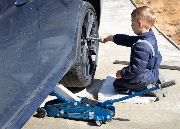 Foto un niño pequeño repara un coche cambia una rueda ayuda a su padre