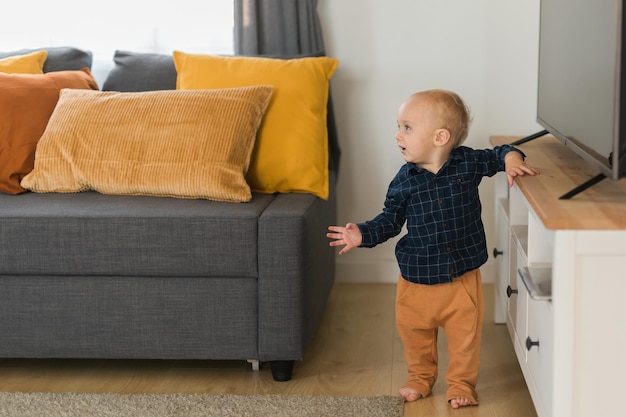 Foto niño pequeño riendo divirtiéndose de pie cerca del sofá en la sala de estar en casa copia espacio adorable bebé m