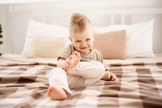 Niño pequeño con ropa beige claro jugando en una cama ligera en casa en el dormitorio comodidad del hogar felicidad de la maternidad bebé en casa