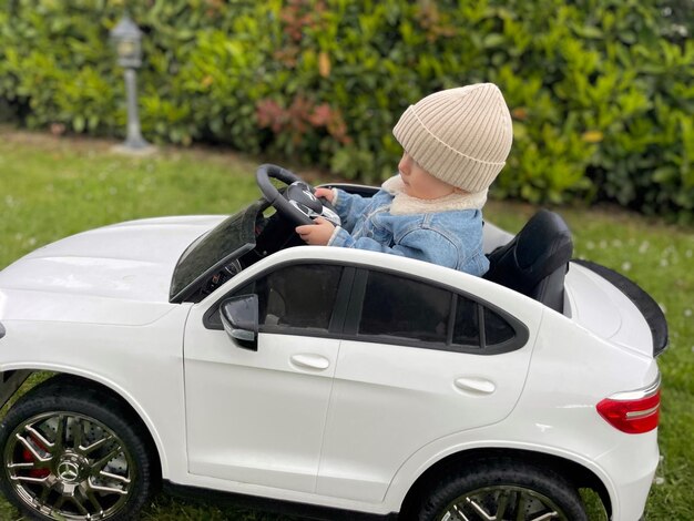 Un niño pequeño con ropa cálida viaja en un gran coche blanco para niños