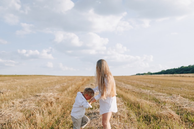 Niño pequeño rubio que juega con la mamá con el pelo blanco con el heno en campo. verano, clima soleado, agricultura. infancia feliz.