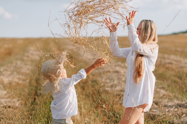 Niño pequeño rubio que juega con la mamá con el pelo blanco con el heno en campo. verano, clima soleado, agricultura. infancia feliz.