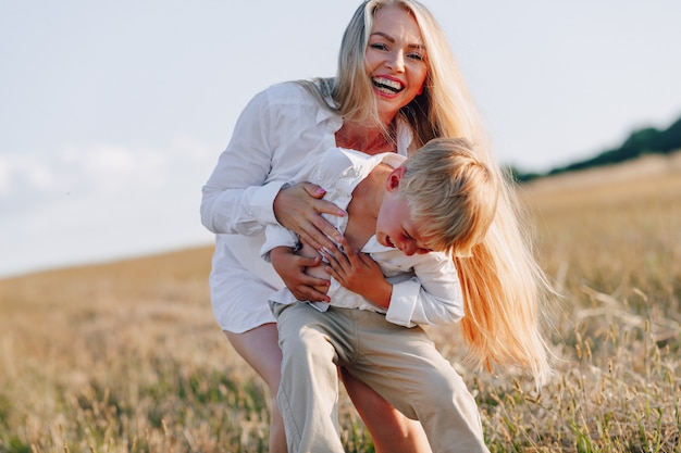 Niño pequeño rubio que juega con la mamá con el pelo blanco con el heno en campo. verano, clima soleado, agricultura. infancia feliz.