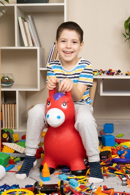 Foto un niño pequeño está saltando sobre un burro de goma inflable entre el desorden en la habitación de los niños.