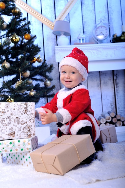 Foto un niño pequeño santa con presente bajo el árbol.