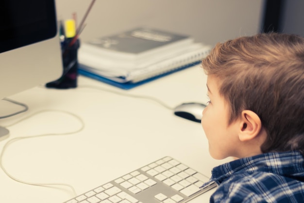 Niño pequeño sentado en el escritorio y usando la computadora en casa