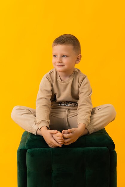 Niño pequeño sentado con las piernas cruzadas sonriendo sobre fondo amarillo