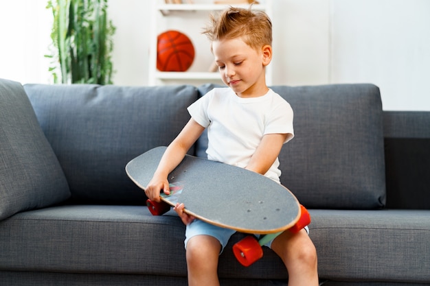 Niño pequeño, sentado, en, sofá, en casa, y, tenencia, patineta, retrato