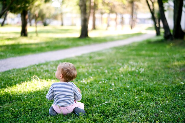 Niño pequeño se sienta en un césped verde cerca de la vista posterior de la pasarela