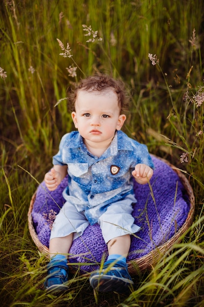 Niño pequeño se sienta en la cesta violeta en el campo verde